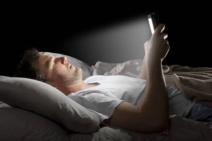 Better Sleep, Best Recovery - Everything You Need To Know About Sleeping Better For Performance 2 Man in bed using screen Guides